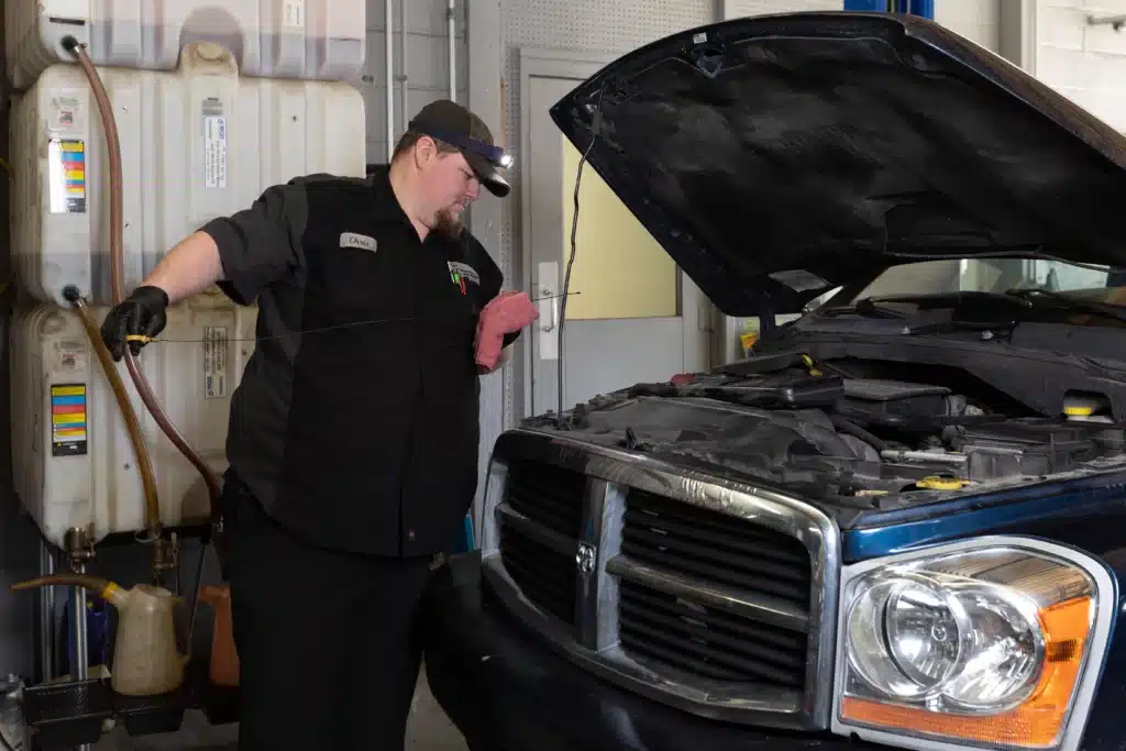 entative Maintenance near me in Merriam, KS with Done With Care Auto Repair Shop. Image of a blue truck with its hood open, as a mechanic from Done With Care Auto Repair Shop checks the oil level using a yellow dipstick.