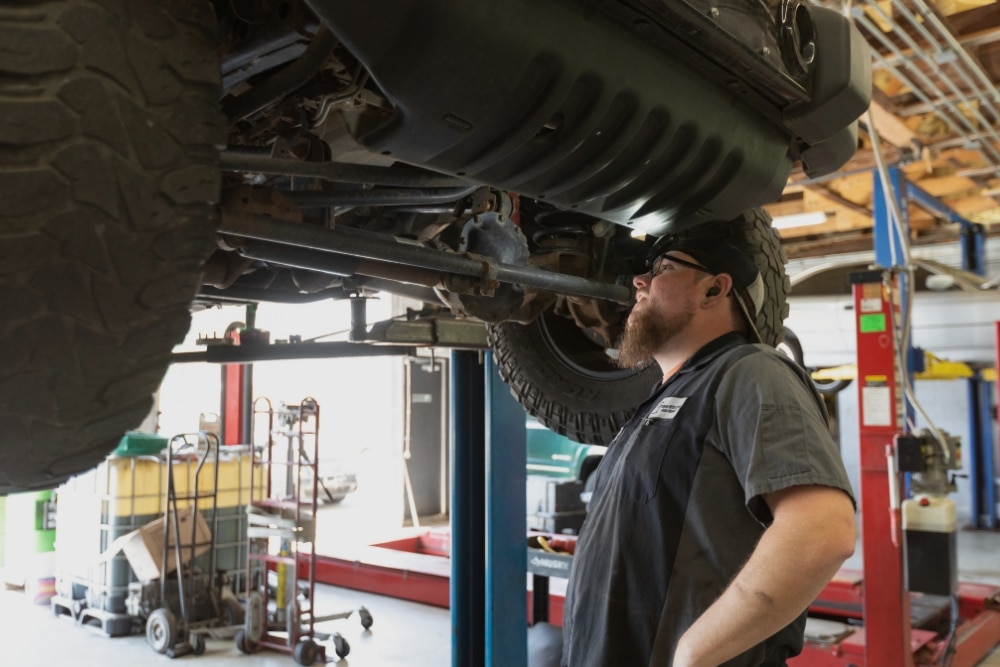 Back-to-School Car Maintenance In Merriam KS At Done With Care Auto Repair. Mechanic inspecting a lifted vehicle in an auto repair shop for maintenance.