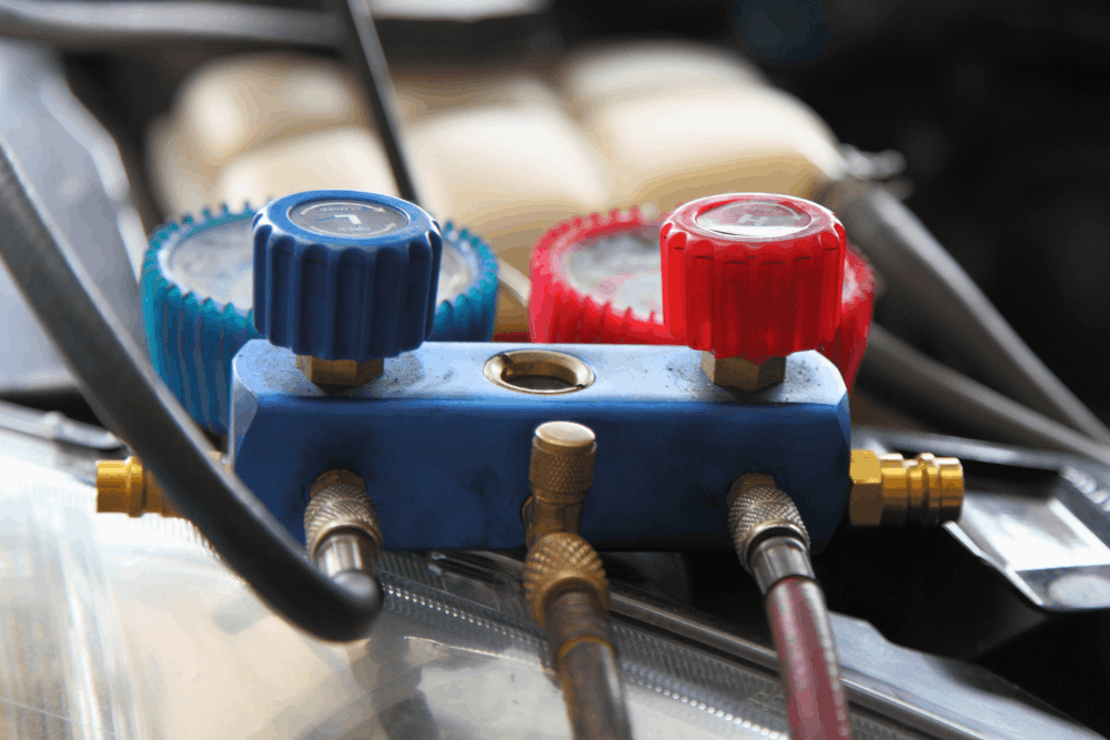 Car A/C test, auto repair in Merriam, KS at Done With Care Auto Repair. Image of red and blue manifold gauges with connected hoses in a vehicle engine bay, used to check air conditioning system pressure and performance.