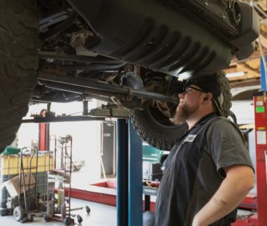 Back-to-School Car Maintenance In Merriam KS At Done With Care Auto Repair. Mechanic inspecting a lifted vehicle in an auto repair shop for maintenance.