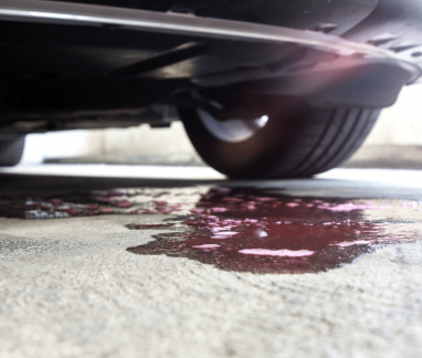 antifreeze leak, auto repair in Merriam, KS at Done With Care Auto Repair. Close-up view of a car leak underneath a vehicle, showing a pool of red fluid on the garage floor, indicating a potential transmission or coolant system issue.