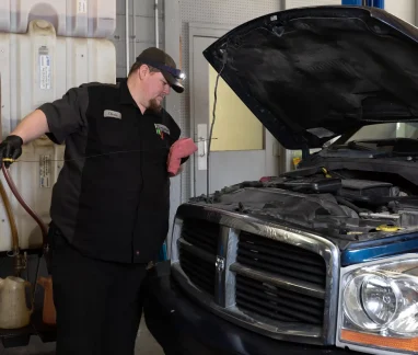entative Maintenance near me in Merriam, KS with Done With Care Auto Repair Shop. Image of a blue truck with its hood open, as a mechanic from Done With Care Auto Repair Shop checks the oil level using a yellow dipstick.